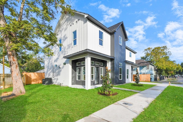 modern farmhouse featuring a front lawn, cooling unit, fence, and board and batten siding