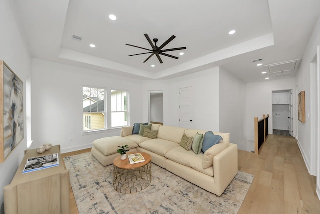 living area with visible vents, attic access, light wood-style floors, and a tray ceiling