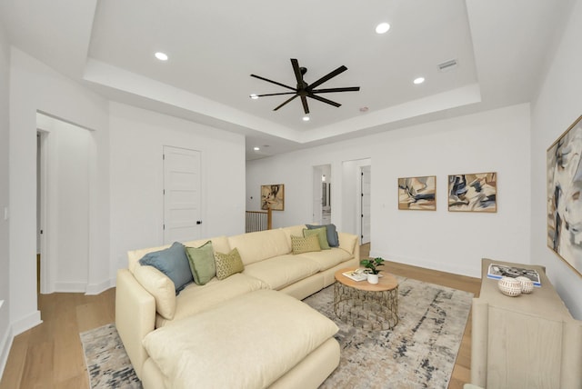 living room featuring a raised ceiling, recessed lighting, wood finished floors, and visible vents