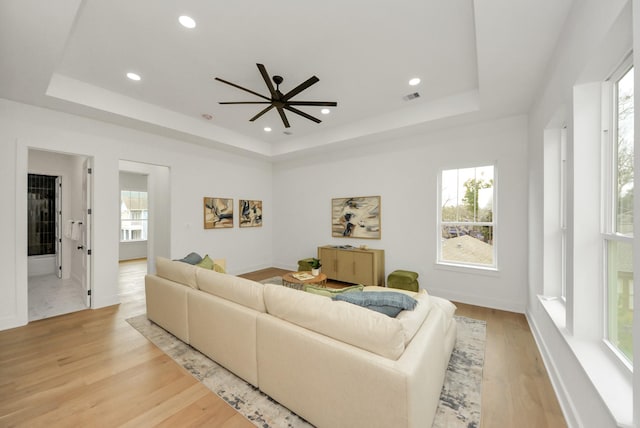 living room with a raised ceiling, recessed lighting, visible vents, and light wood finished floors