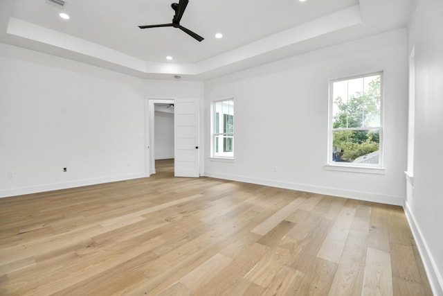 empty room featuring recessed lighting, baseboards, a raised ceiling, and light wood-style floors