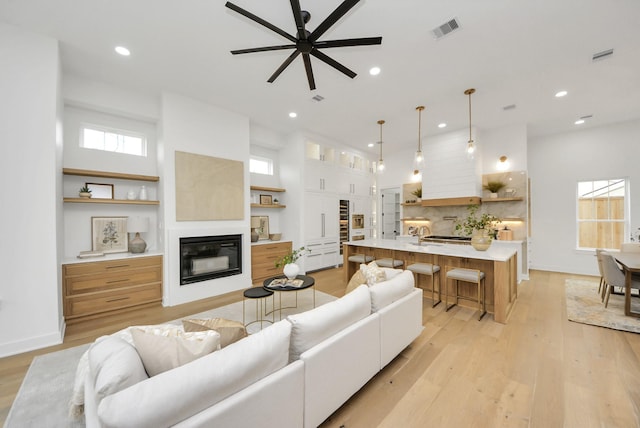 living room with light wood-type flooring, visible vents, a glass covered fireplace, and recessed lighting