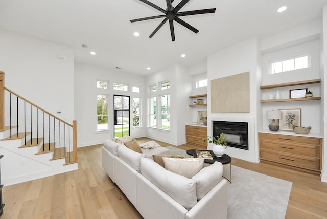 living room with a glass covered fireplace, recessed lighting, stairway, light wood-style floors, and baseboards