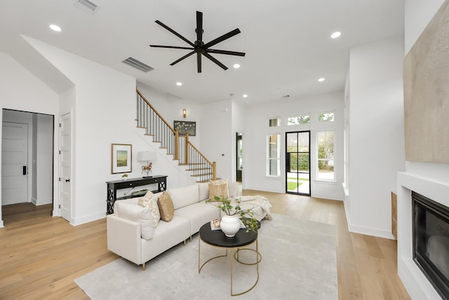 living room featuring visible vents, a glass covered fireplace, stairs, and light wood finished floors