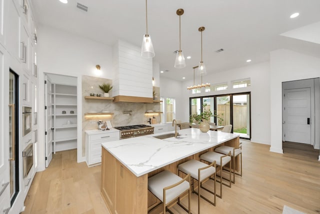 kitchen featuring visible vents, light wood-style flooring, a sink, decorative backsplash, and appliances with stainless steel finishes