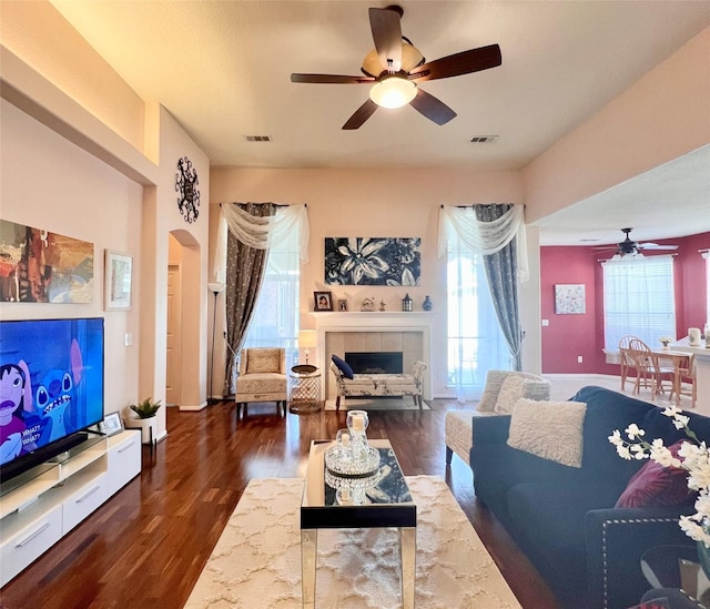 living room with visible vents, arched walkways, wood finished floors, and a tile fireplace