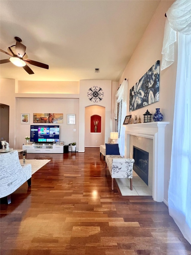 living room featuring a tiled fireplace, wood finished floors, visible vents, and a ceiling fan