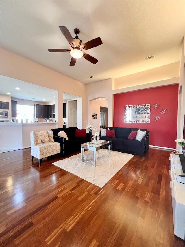 living area with dark wood-type flooring, arched walkways, visible vents, and ceiling fan