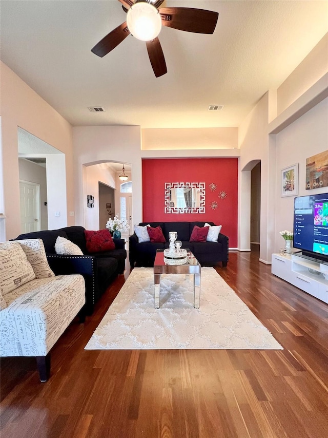 living area with ceiling fan, visible vents, arched walkways, and wood finished floors