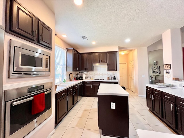 kitchen with visible vents, a kitchen island, light countertops, appliances with stainless steel finishes, and tasteful backsplash