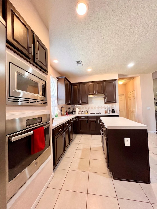 kitchen with visible vents, a kitchen island, light countertops, light tile patterned floors, and stainless steel appliances