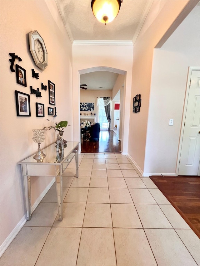 corridor featuring arched walkways, ornamental molding, baseboards, and light tile patterned flooring