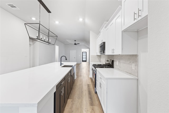 kitchen featuring light countertops, decorative backsplash, appliances with stainless steel finishes, light wood-style floors, and a sink