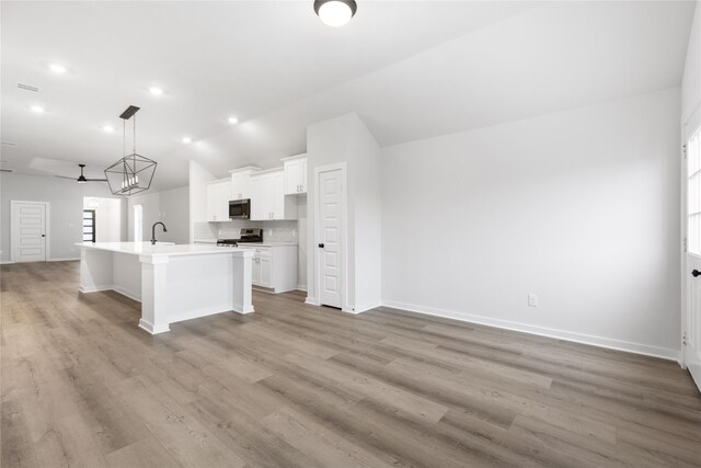 kitchen featuring a center island with sink, open floor plan, stainless steel appliances, white cabinets, and lofted ceiling