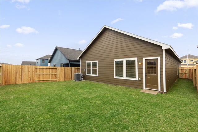 rear view of property featuring central air condition unit, a lawn, and a fenced backyard