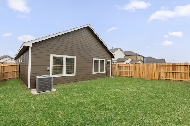 rear view of property featuring central air condition unit, a yard, and a fenced backyard