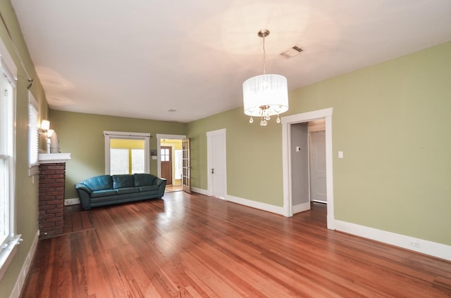 unfurnished living room featuring a chandelier, visible vents, baseboards, and wood finished floors