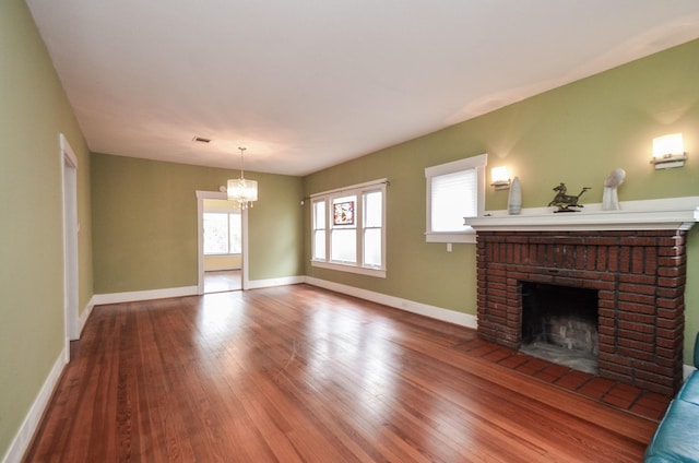 unfurnished living room with baseboards, a notable chandelier, a brick fireplace, and wood finished floors