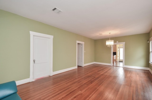 empty room with a notable chandelier, wood finished floors, visible vents, and baseboards