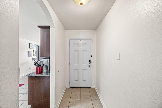 doorway to outside with light tile patterned floors, baseboards, arched walkways, and a textured ceiling