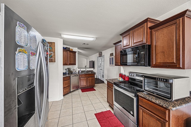 kitchen with light tile patterned floors, dark stone counters, appliances with stainless steel finishes, and a toaster