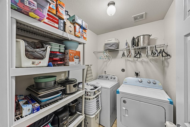 clothes washing area with laundry area, washing machine and dryer, a textured ceiling, and visible vents