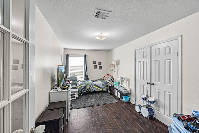 bedroom featuring visible vents, a textured ceiling, dark wood-style floors, a closet, and a textured wall