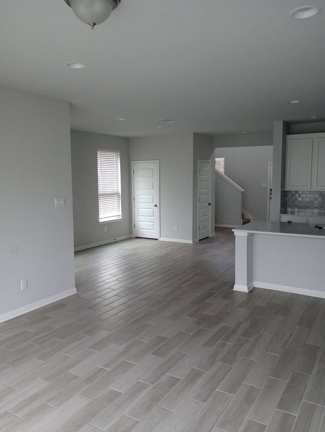 unfurnished living room featuring stairway, baseboards, and light wood finished floors