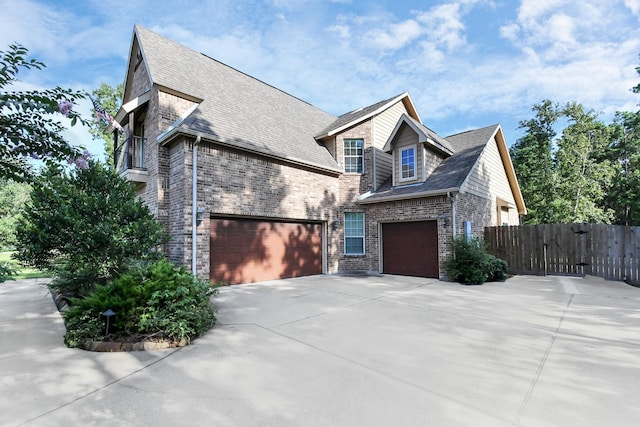 view of side of property featuring brick siding, fence, roof with shingles, driveway, and a gate