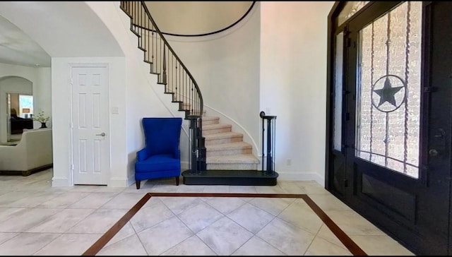 foyer with stairway, baseboards, arched walkways, and tile patterned flooring