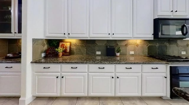 kitchen with black appliances, decorative backsplash, dark stone counters, white cabinets, and glass insert cabinets