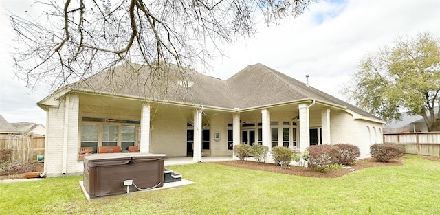 back of house featuring a yard, fence, brick siding, and a hot tub