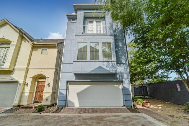 view of front facade with stucco siding, an attached garage, decorative driveway, and a balcony