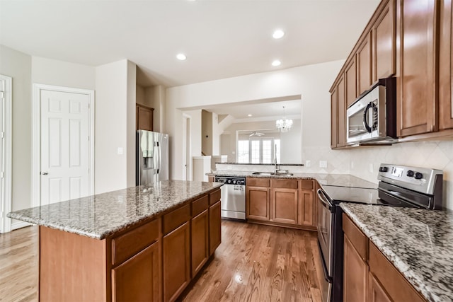 kitchen with light stone counters, brown cabinetry, a sink, appliances with stainless steel finishes, and light wood-type flooring