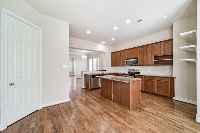 kitchen with visible vents, a kitchen island, appliances with stainless steel finishes, a peninsula, and brown cabinetry