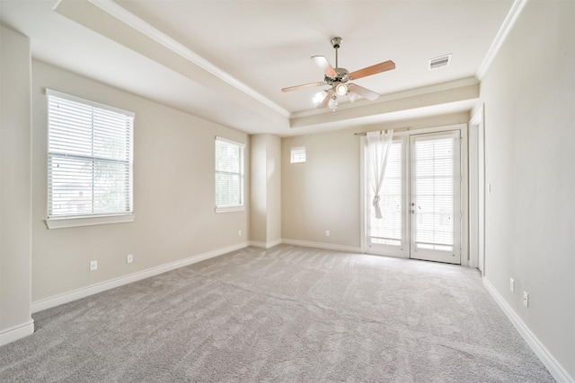 carpeted empty room with a raised ceiling, a ceiling fan, baseboards, and ornamental molding