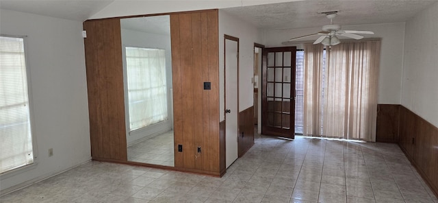 unfurnished room with plenty of natural light, wood walls, a textured ceiling, and ceiling fan