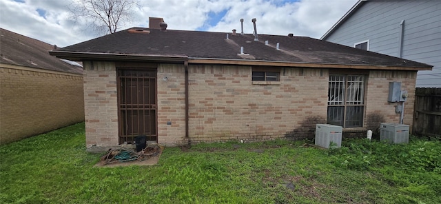 back of property featuring brick siding, a shingled roof, a yard, and fence