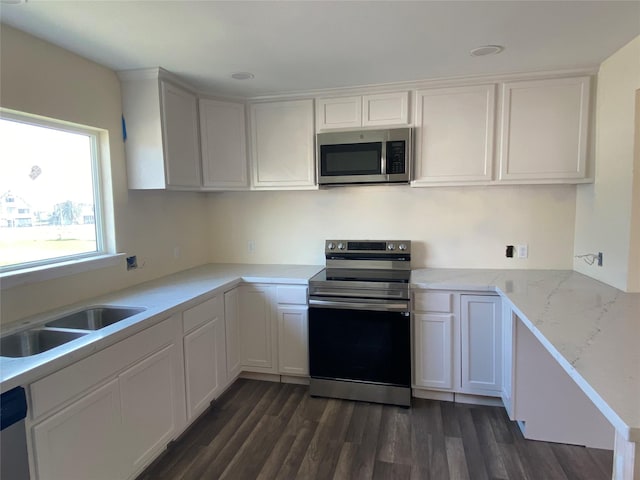 kitchen featuring light stone countertops, a sink, dark wood-type flooring, appliances with stainless steel finishes, and white cabinetry