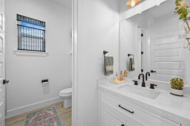 bathroom with baseboards, toilet, wood finished floors, and vanity