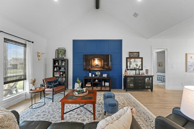 living area featuring beam ceiling, a healthy amount of sunlight, visible vents, and light wood-type flooring