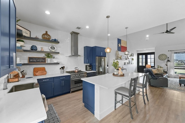 kitchen with a sink, wall chimney exhaust hood, blue cabinets, and stainless steel appliances