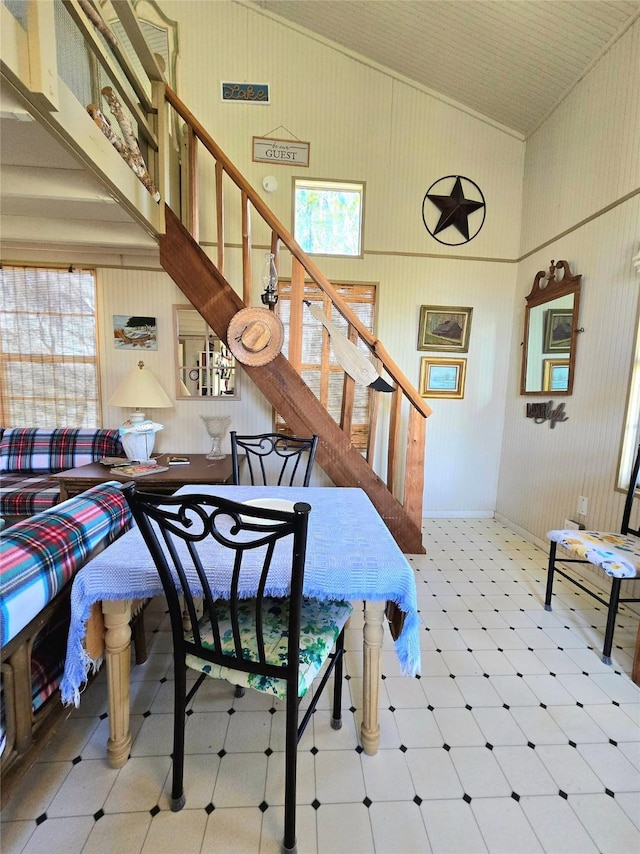 dining area with tile patterned floors, high vaulted ceiling, and stairs