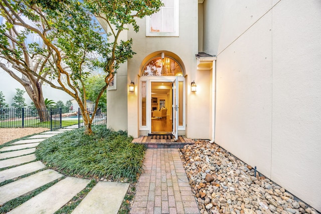 view of exterior entry featuring stucco siding and fence