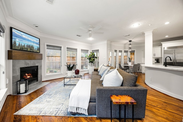 living area with a tiled fireplace, crown molding, wood finished floors, and ornate columns