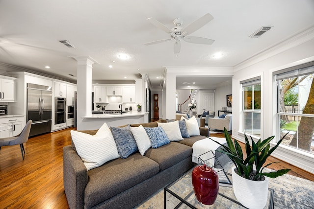 living area featuring visible vents, dark wood-type flooring, crown molding, and decorative columns