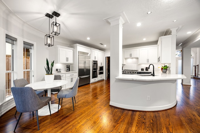 kitchen with decorative columns, dark wood-style flooring, ornamental molding, stove, and stainless steel built in refrigerator