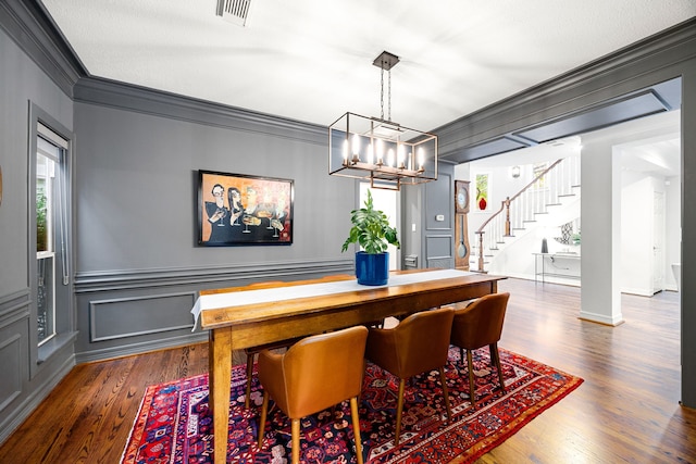 dining space with visible vents, crown molding, stairs, a decorative wall, and dark wood-style flooring