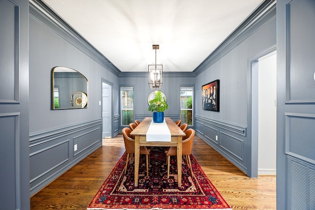 dining area with an inviting chandelier, wood finished floors, and ornamental molding