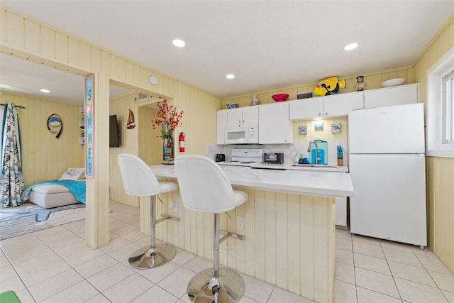 kitchen featuring a breakfast bar, white appliances, light tile patterned floors, and light countertops